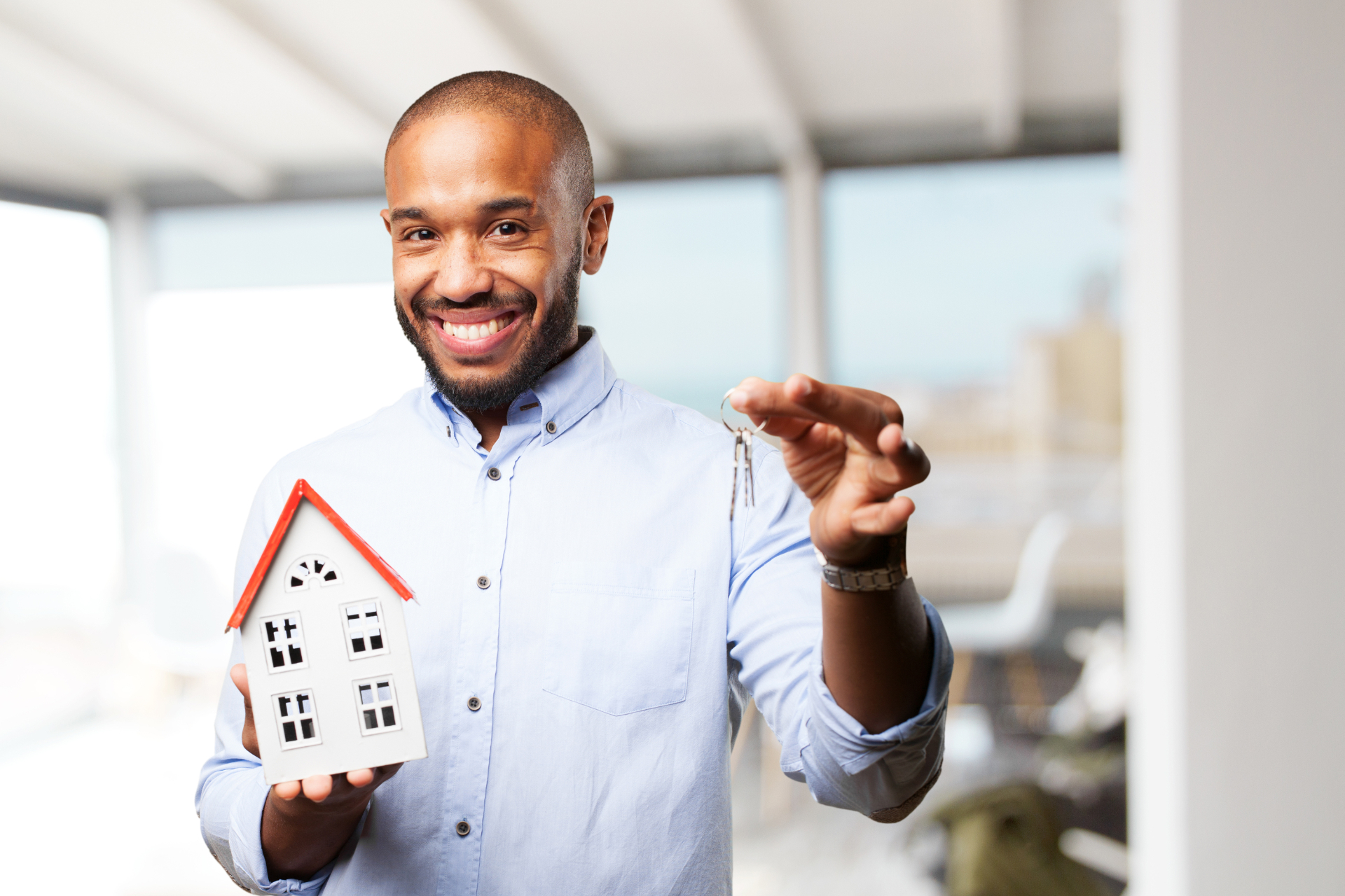 A smiling man holding a model house and a set of keys